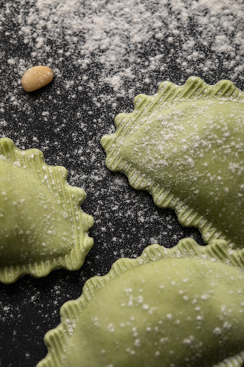 close up view of green ravioli with flour and pine nut on black table