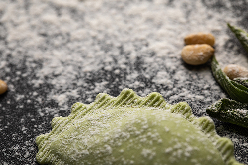 selective focus of green ravioli and scattered flour on black table