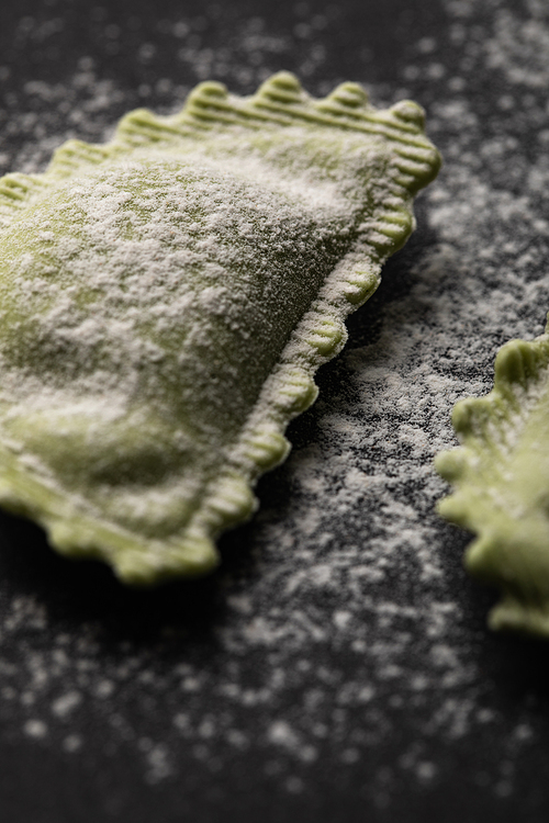 close up view of green fresh raw ravioli with flour on black table