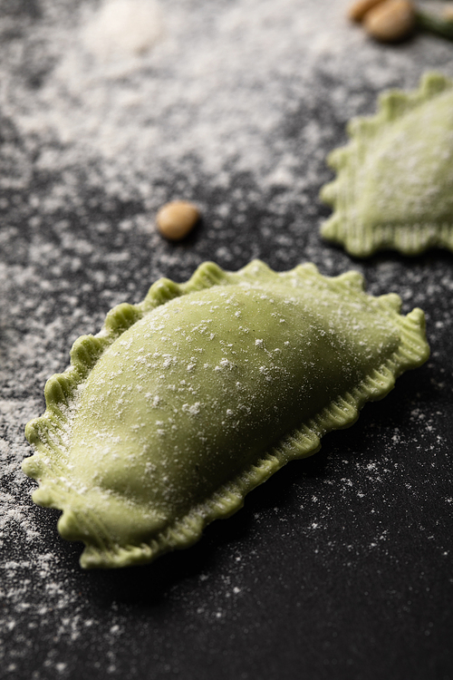 close up view of green uncooked ravioli with flour on black table