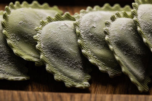 close up view of raw green ravioli on wooden board