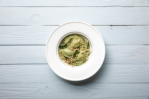 top view of plate with green ravioli with pine nuts and sage at wooden table