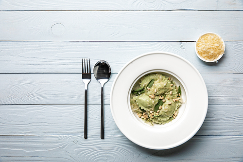 top view of green ravioli with pine nuts and sage served with grated cheese at wooden table