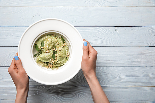 cropped view of woman holding plate with green ravioli with pine nuts and sage at wooden table