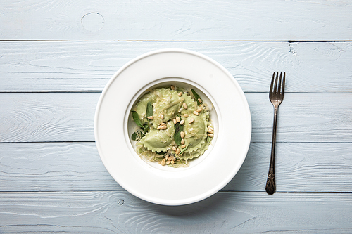 top view of plate with green ravioli with pine nuts and sage at wooden table near fork