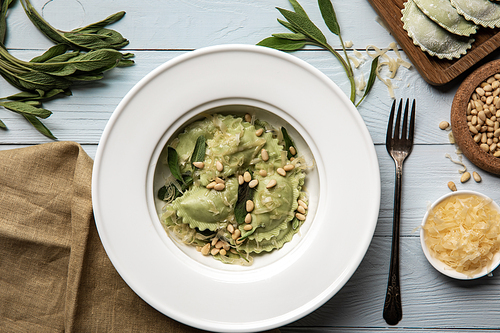 top view of green ravioli served in white plate with pine nuts, sage and grated cheese