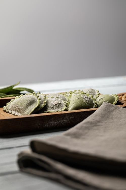 selective focus of raw green ravioli served on wooden board near napkin isolated on grey