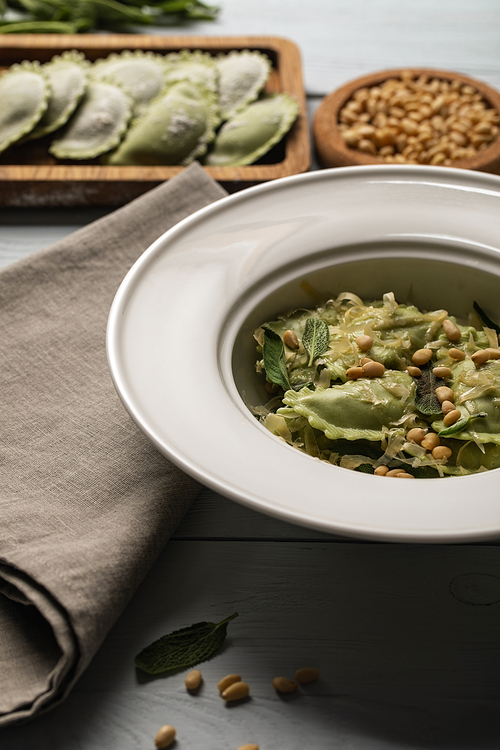 close up view of green ravioli served in plate with sage, pine nuts and grated cheese near napkin