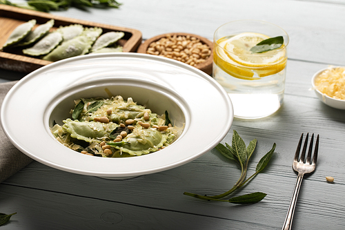 green ravioli with pine nuts, grated cheese and sage at wooden table near water with lemon