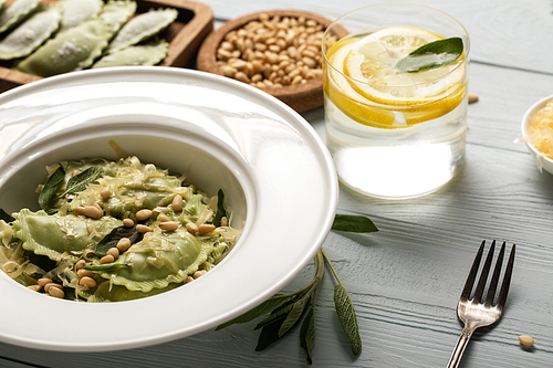 close up view of green ravioli with pine nuts, grated cheese and sage at wooden table near water with lemon