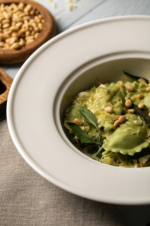 close up view of ravioli served in plate with sage, pine nuts and grated cheese near napkin