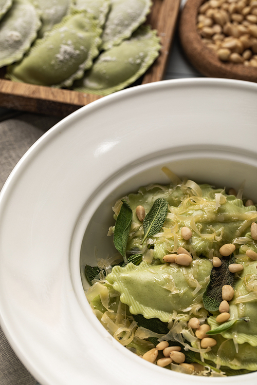 close up view of tasty green ravioli served in plate with sage, pine nuts and grated cheese