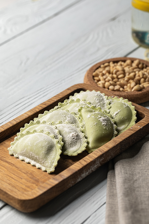 close up view of raw green ravioli with flour on wooden board near pine nuts