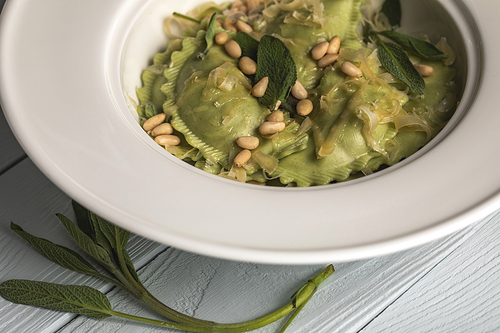 close up view of delicious ravioli with melted cheese, pine nuts and sage on wooden table