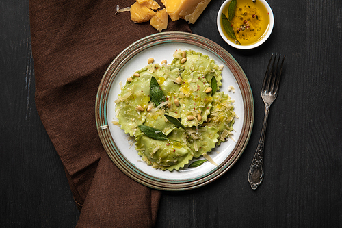 top view of green ravioli served in vintage plate near silver fork at black wooden table