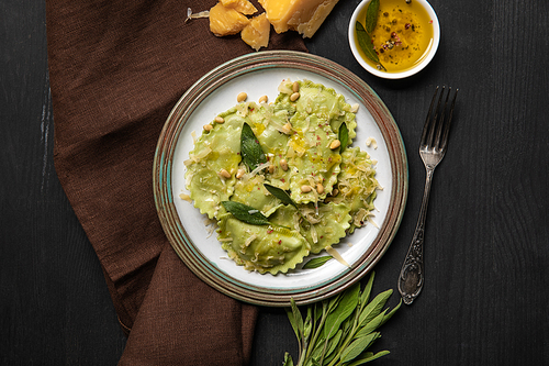 top view of green ravioli served in vintage plate near silver fork and napkin at black wooden table