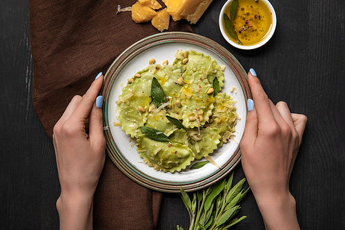 top view of woman holding plate with delicious ravioli at black wooden table