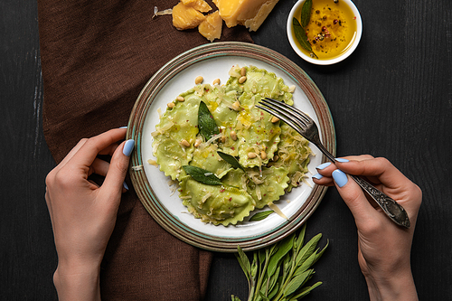 top view of woman eating delicious green ravioli with sage and pine nuts at black wooden table