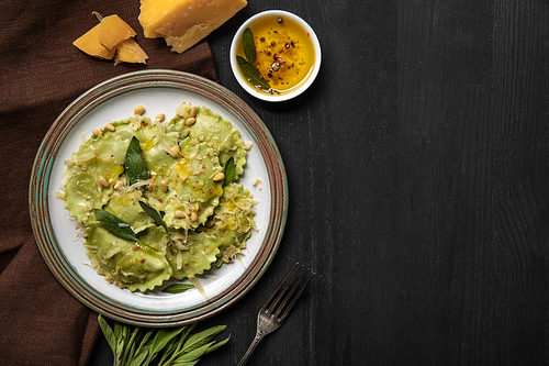 top view of green ravioli served in vintage plate near silver fork at black wooden table with copy space