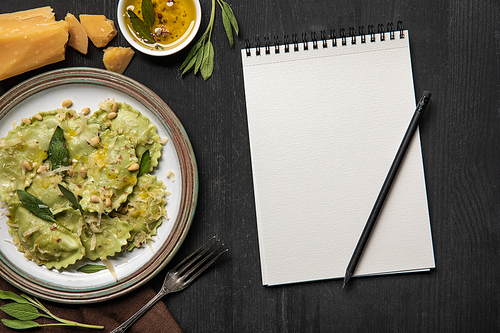 top view of served ravioli and empty white notebook with pencil