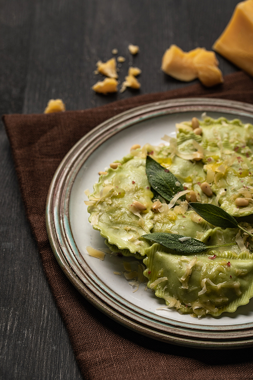 close up view of tasty green ravioli with sage, cheese and pine nuts served on black wooden table with brown napkin