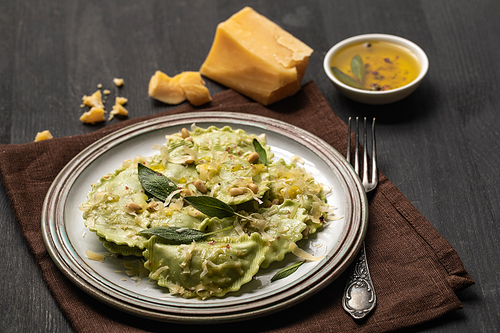 delicious green ravioli with sage, cheese and pine nuts served on black wooden table with fork and napkin