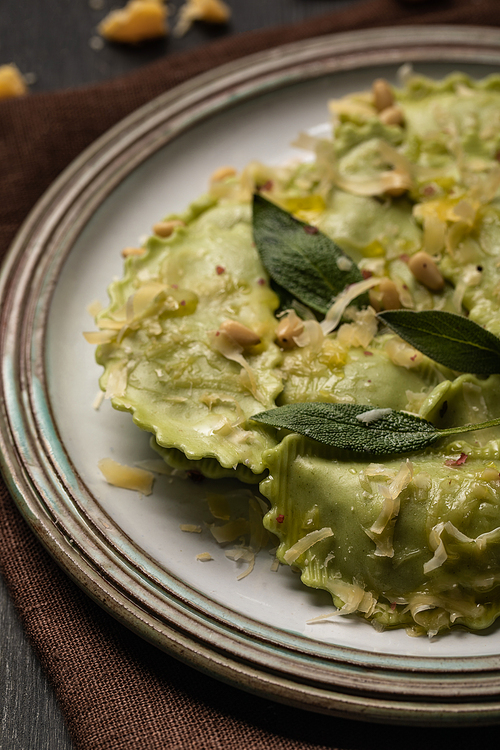 close up view of green ravioli with melted cheese, pine nuts and green sage leaves in retro plate