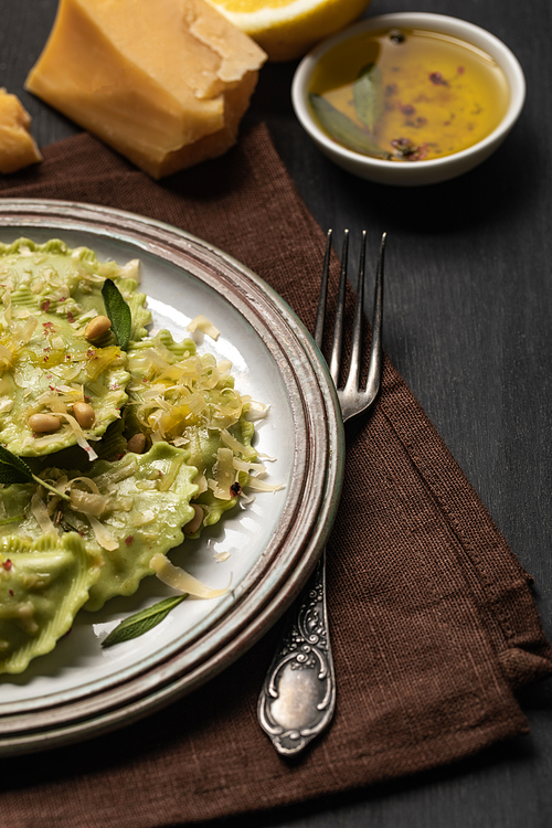 close up view of delicious green ravioli with sage, cheese and pine nuts served on black wooden table with fork and napkin