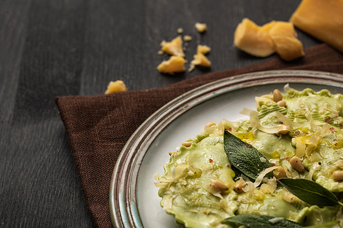 close up view of delicious green ravioli with sage, cheese and pine nuts served on black wooden table with brown napkin