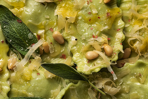 close up view of green ravioli with melted cheese, pine nuts and green sage leaves