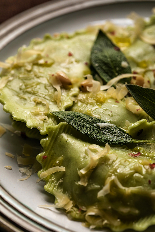 close up view of green ravioli with melted cheese, pine nuts and green sage leaves on plate