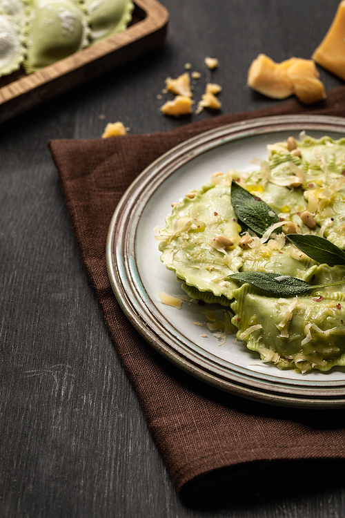 close up view of green ravioli with melted cheese, pine nuts and green sage leaves in retro plate