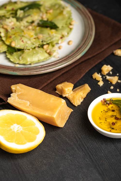 selective focus of green ravioli on plate near lemon half, cheese and spicy oil