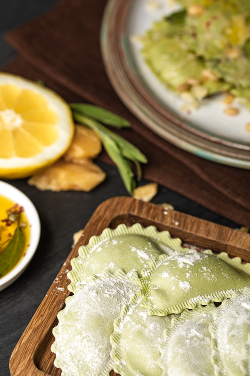 selective focus of green raw ravioli with flour on wooden board