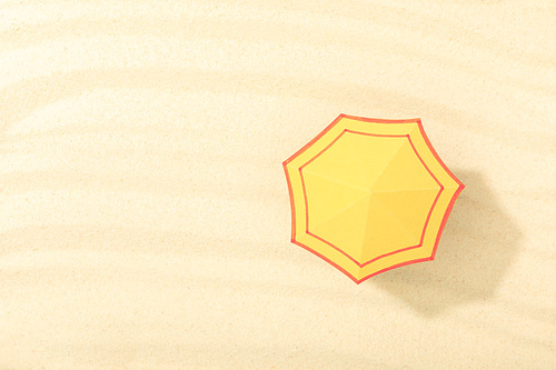 top view of paper beach with yellow umbrella on textured sand