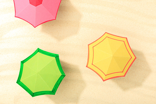 top view of paper beach with multicolored umbrellas on textured sand