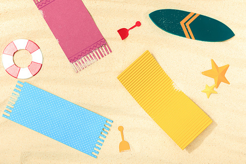 top view of paper beach with surfboard and towels on textured sand