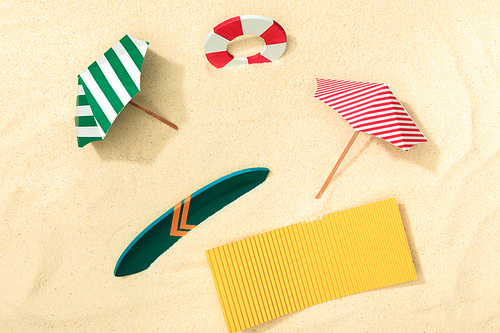 top view of paper beach with lifebuoy, umbrellas, surfboard and towel on textured sand