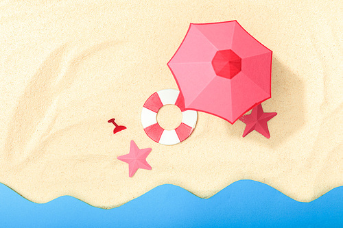 top view of paper beach with lifebuoy, pink umbrella and starfishes on textured sand near ocean