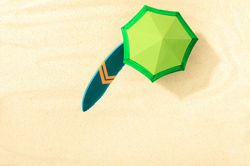 top view of paper beach with green umbrella and surfboard on textured sand