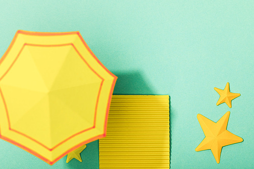 top view of paper yellow towel and umbrella near starfishes on turquoise background