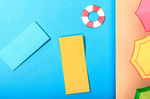 top view of paper calm blue sea with pool floats and lifebuoy and umbrellas on shore