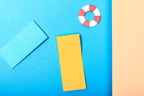 top view of paper calm blue sea with pool floats and lifebuoy and empty shore