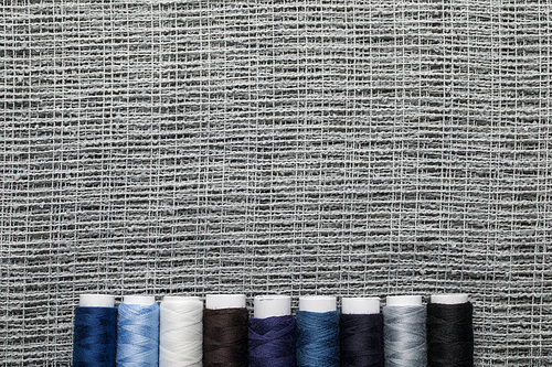 top view of blue and grey thread coils in row on sackcloth with copy space