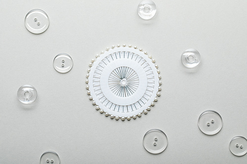 top view of transparent clothing buttons and round container with sewing pins isolated on grey