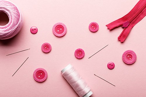 top view of clothing buttons, thread coil and sewing supplies isolated on pink