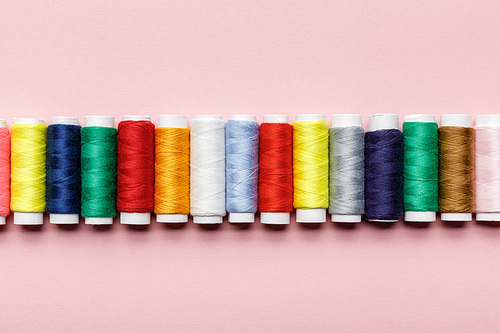 top view of colorful thread coils in row on pink