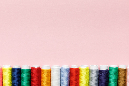 top view of colorful thread coils in row isolated on pink with copy space