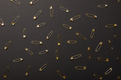 top view of scattered metal safety pins isolated on black