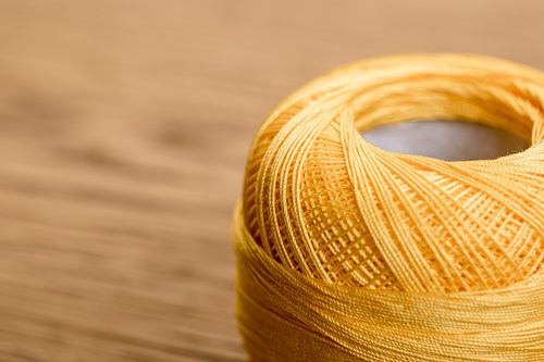 selective focus of yellow cotton knitting yarn ball on wooden table with copy space